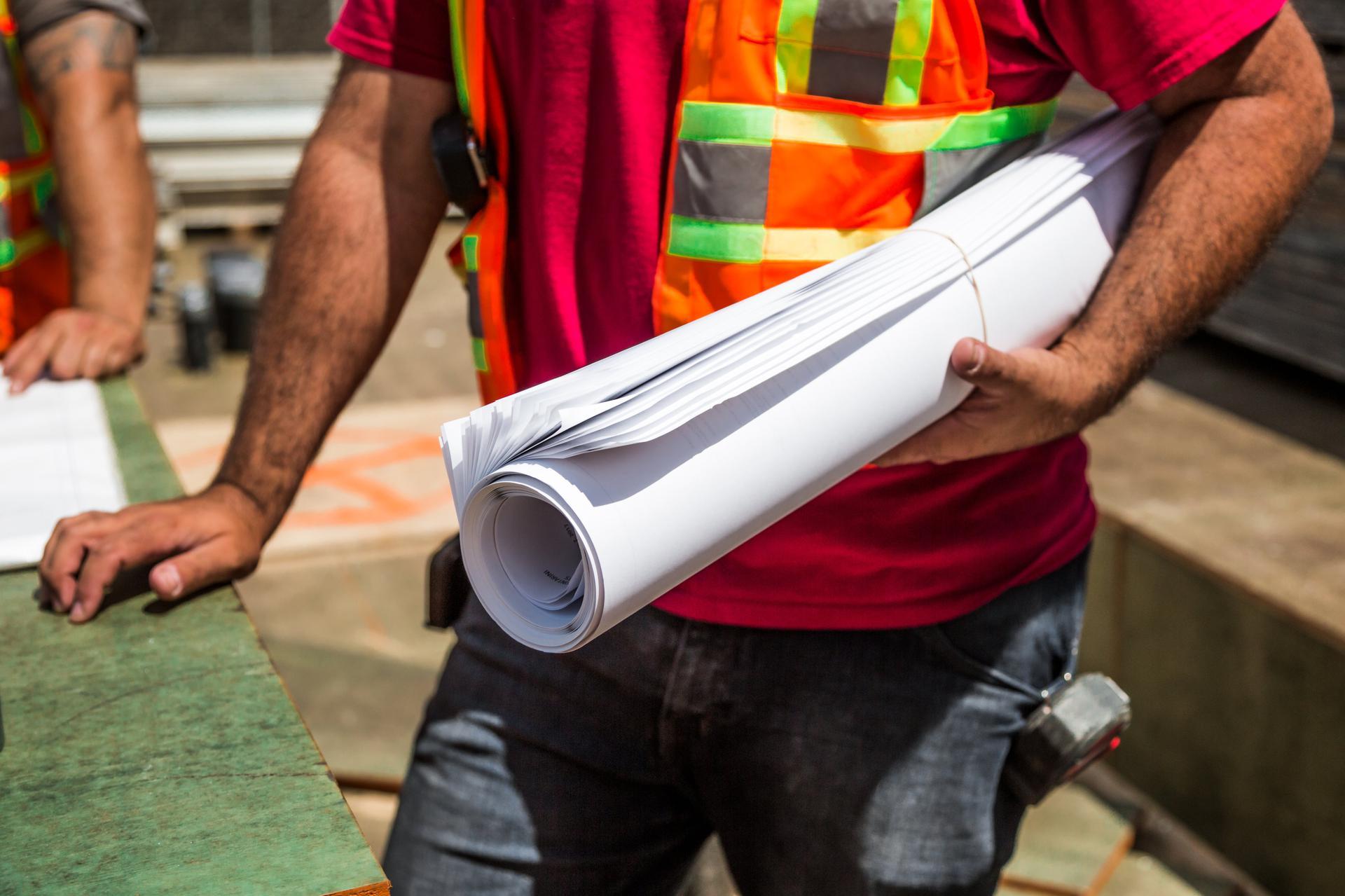 Contractor holding rolled construction blueprints on a job site